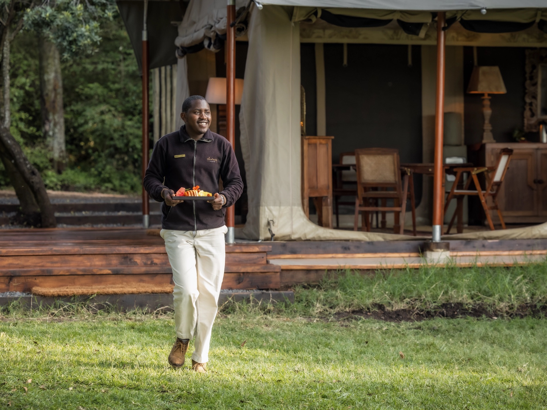 A member of camp staff carrying a breakfast tray across the grass to a tent