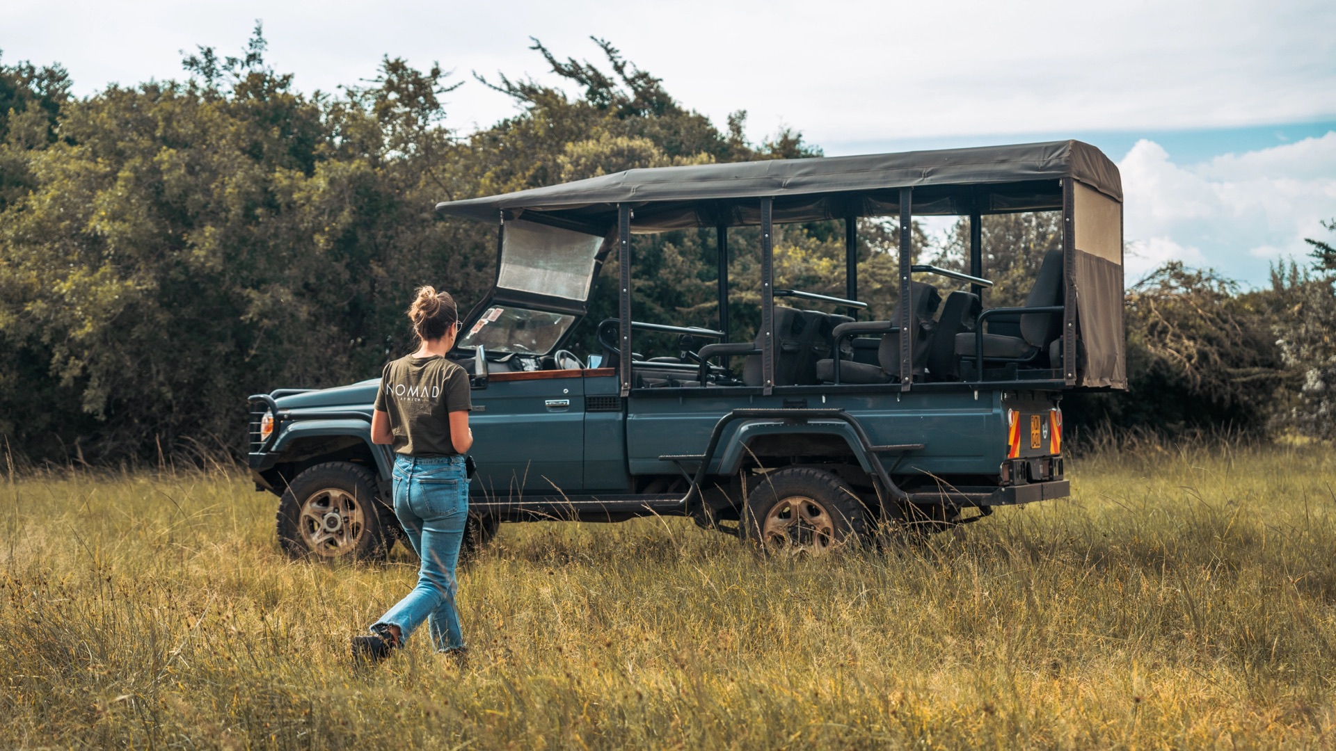 A woman walking towards an open-sided safari vehicle in long grass