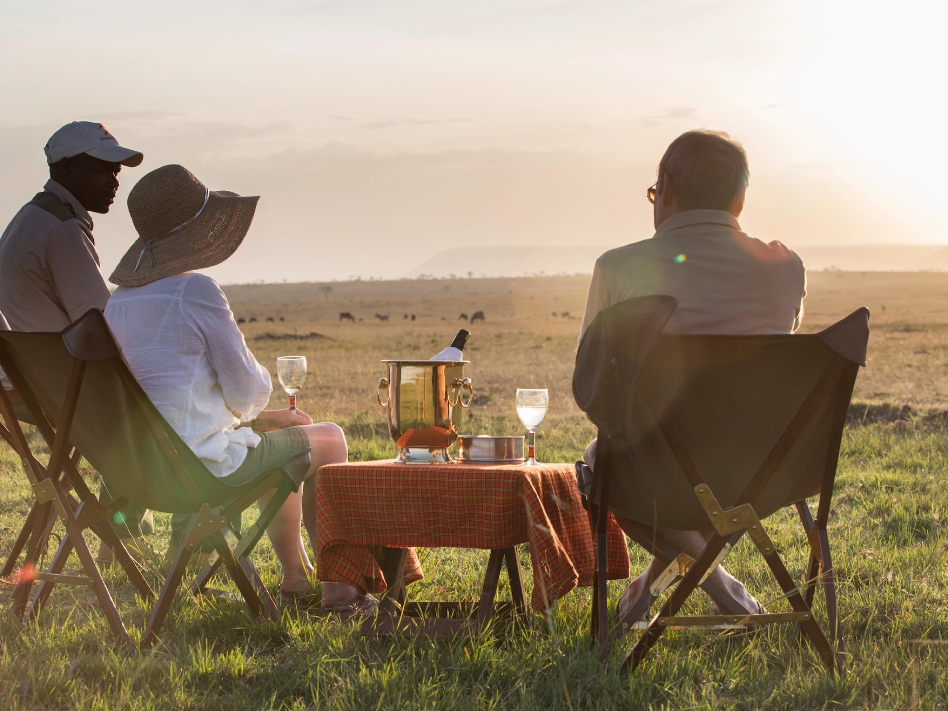Four people in camp chairs watching the plains at sunset, a table of drinks beside them